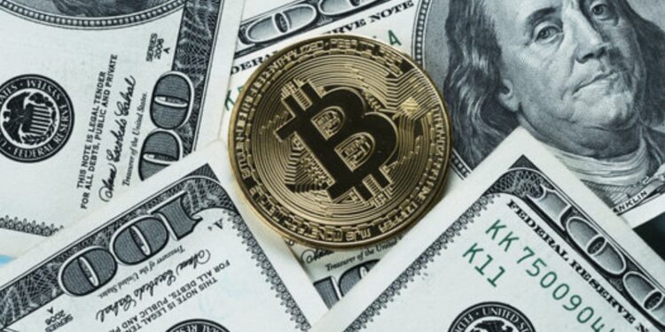 Moneda física de bitcoin dorada rodeada de billetes físicos de 100 dólares.
