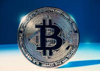 Moneda física de bitcoin dorada sobre una mesa blanca y fondo azul.