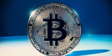 Moneda física de bitcoin dorada sobre una mesa blanca y fondo azul.