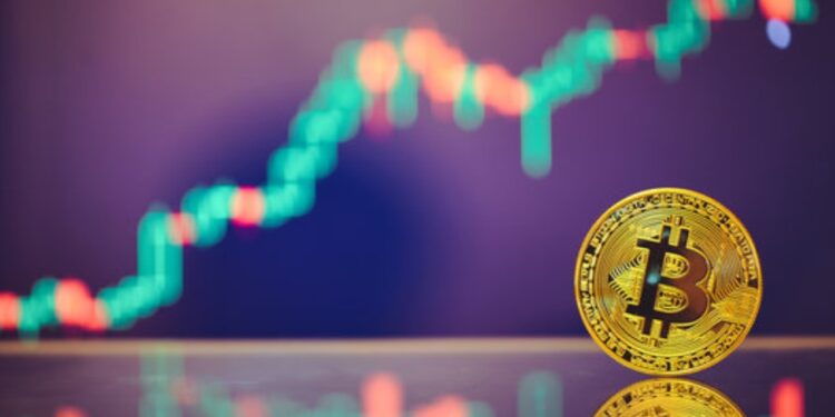 Moneda física de bitcoin doarada sobre un espejo y con gráficas de mercado en el fondo.