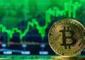 Moneda física de bitcoin dorada con gráficas verdes en el fondo.