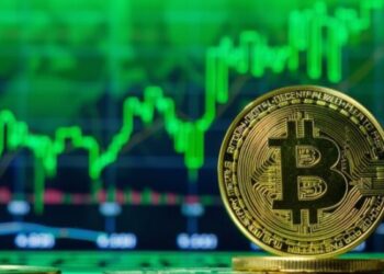 Moneda física de bitcoin dorada con gráficas verdes en el fondo.