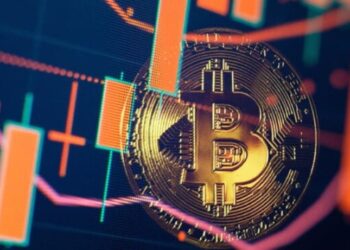 Moneda física de bitcoin dorada con velas de gráficos alrededor.