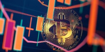Moneda física de bitcoin dorada con velas de gráficos alrededor.