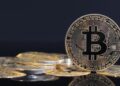 Moneda física de bitcoin dorada sobre un escritorio con fondo negro.