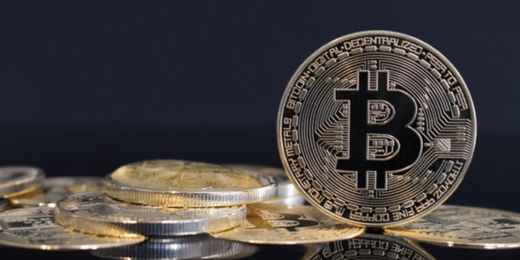 Moneda física de bitcoin dorada sobre un escritorio con fondo negro.