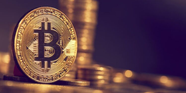 Moneda física dorada de bitcoin con otras monedas apiladas detrás en fondo púrpura.
