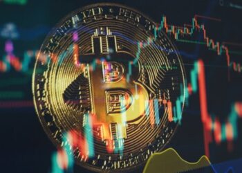 Moneda física de bitcoin dorada con gráficos de mercados alrededor.