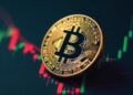 Moneda física de bitcoin dorada sobre gráficos de mercado con velas rojas y verdes.