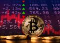 Monedas físicas de bitcoin doradas sobre un escritorio con una gráfica en rojo y números en el fondo.