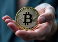Moneda física de bitcoin dorada en una mano humana extendida con fondo borroso.