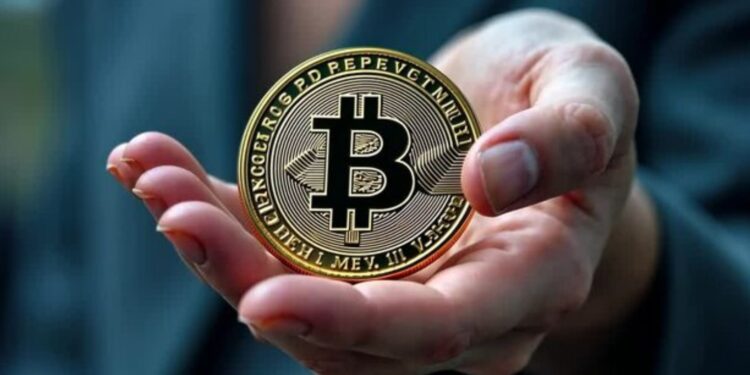 Moneda física de bitcoin dorada en una mano humana extendida con fondo borroso.