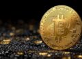 Moneda física de bitcoin dorada con suelo de piedras y fondo negro.