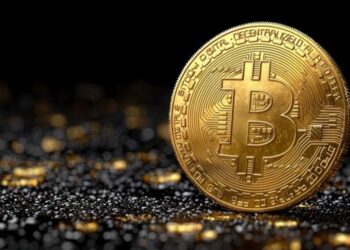 Moneda física de bitcoin dorada con suelo de piedras y fondo negro.