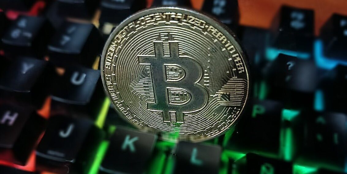 Moneda física de bitcoin dorada sobre un teclado de computadora.
