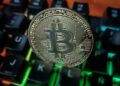 Moneda física de bitcoin dorada sobre un teclado de computadora.