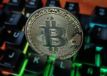 Moneda física de bitcoin dorada sobre un teclado de computadora.