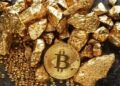 Una moneda física de bitcoin dorada rodeada de trozos de oro sobre una mesa.