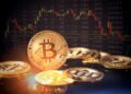 Monedas físicas de bitcoin sobre un escritorio con gráficas de fondo.