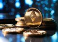 Moneda física dorada de ETH junto a otra sobre un escritorio.