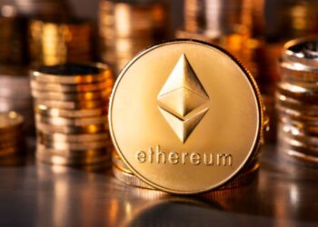 Moneda física de ether en un escritorio con más monedas apiladas en el fondo.