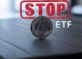 Moneda física de litecoin plateada sobre un un escritorio con las letras ETF al lado y en la parte superior un sello con la palabra stop en rojo.
