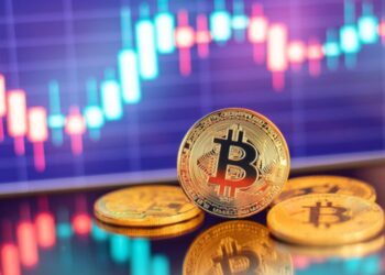 Monedas físicas de BTC sobre un escritorio con fondo morado que tiene gráficas verdes y rojas brillantes.