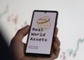 Un celular muestra en su pantalla las palabras Real World Assets.