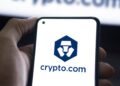 Mano sujetando un teléfono que muestra el logo de Crypto.com.
