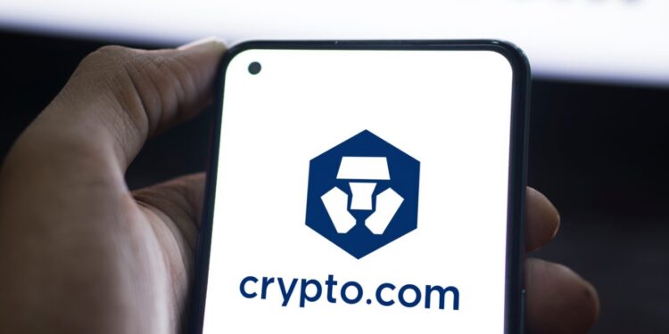 Mano sujetando un telรฉfono que muestra el logo de Crypto.com.