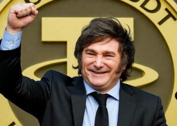 Imagen realista del presidente argentino Javier Milei en pose triunfante, levantando el puño con una sonrisa victoriosa, frente a un fondo con una gran moneda dorada de USDT (Tether), evocando temas de economía y criptomonedas.