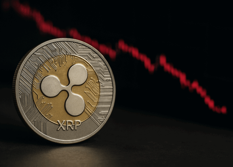 Una moneda física de Ripple (XRP) en primer plano, con diseño dorado y plateado, y al fondo un gráfico de velas rojas en caída que representa la bajada de su precio en el mercado.