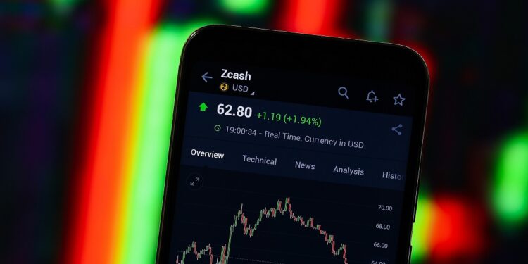 Un teléfono móvil mostrando gráficos de precio de Zcash en su pantalla con un gráfico de fondo.