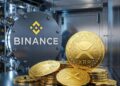 Varias monedas físicas doradas con el logo de XRP apiladas y esparcidas dentro de una bóveda de Binance.