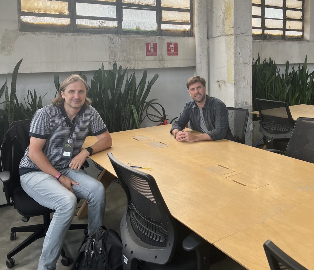 Foto de Bartek Kiepuszewski conversando en una mesa con el reportero Franco Scandizzo de CriptoNoticias.