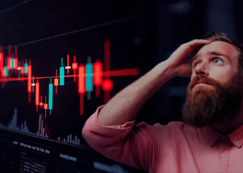 Gráfico de velas del mercado en rojo, hombre preocupado agarrandose la cabeza indeciso