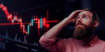 Gráfico de velas del mercado en rojo, hombre preocupado agarrandose la cabeza indeciso