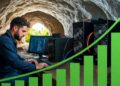 Un minero trabajando en una cueva con equipos de computación, junto a un gráfico de barras creciente.