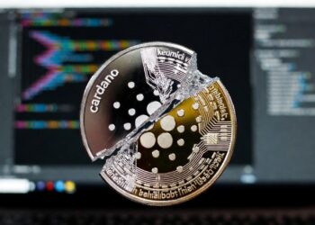 Una moneda digital e Cardano partida en pedazos con un fondo de una pantalla de una computadora.