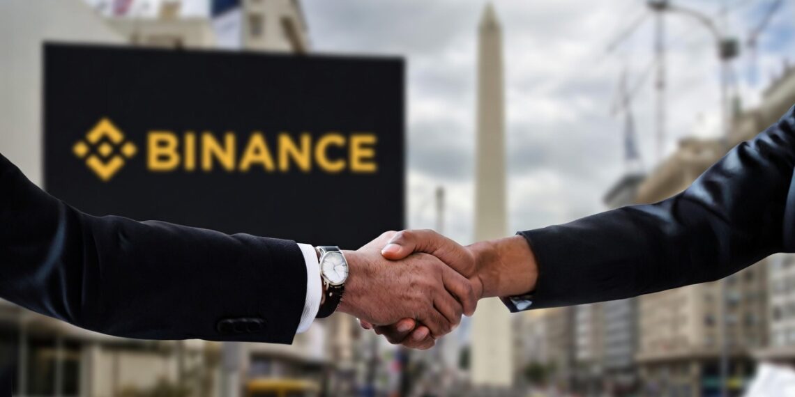 Foto de dos manos estrechadas y formando un acuerdo, al fondo se observa un cartel de Binance y el obelisco de Buenos Aires.