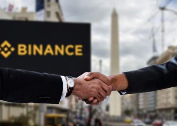 Foto de dos manos estrechadas y formando un acuerdo, al fondo se observa un cartel de Binance y el obelisco de Buenos Aires.
