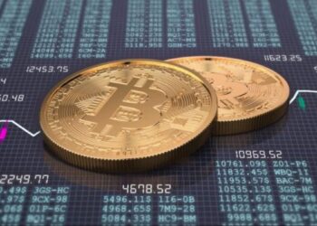 Monedas físicas de bitcoin doradas sobre un escritorio que tiene gráficas e información de mercado.