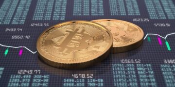 Monedas físicas de bitcoin doradas sobre un escritorio que tiene gráficas e información de mercado.