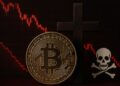 Moneda física de bitcoin dorada con una cruz al lado, un símbolo de muerte y gráficas rojas.