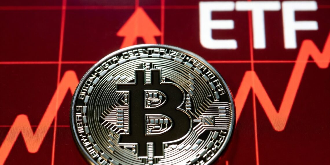 Moneda física de bitcoin en primer plano, detrás un gráfico financiero en rojo intenso y las letras ETF.