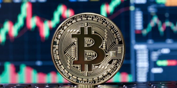Una moneda física de bitcoin con un fondo con gráficos bursátiles en rojo y verde.