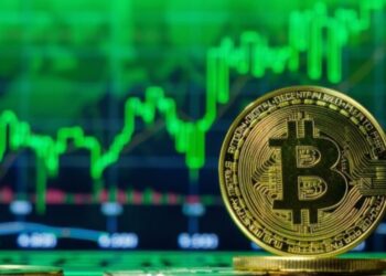 Moneda física de bitcoin dorada con gráficas verdes en el fondo.