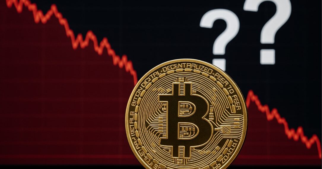 Moneda física de bitcoin dorada con gráficas rojas y signos de interrogación.