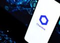 Smartphone apoyado sobre el teclado de un portátil y en la pantalla del móvil aparece el logo oficial de Chainlink.