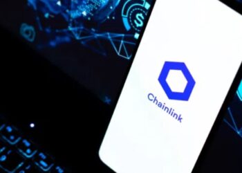 Smartphone apoyado sobre el teclado de un portátil y en la pantalla del móvil aparece el logo oficial de Chainlink.